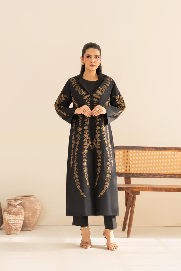 Woman wearing a black embroidered kurta with gold details against a beige background